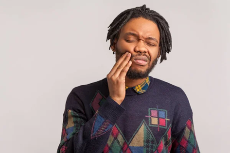 A man touches his cheek, wincing in pain from cavities.