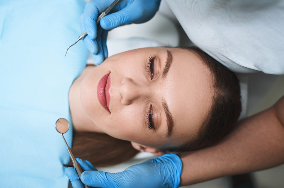 Woman receiving dental care as a dentist in blue gloves uses a dental mirror and probe near her teeth.