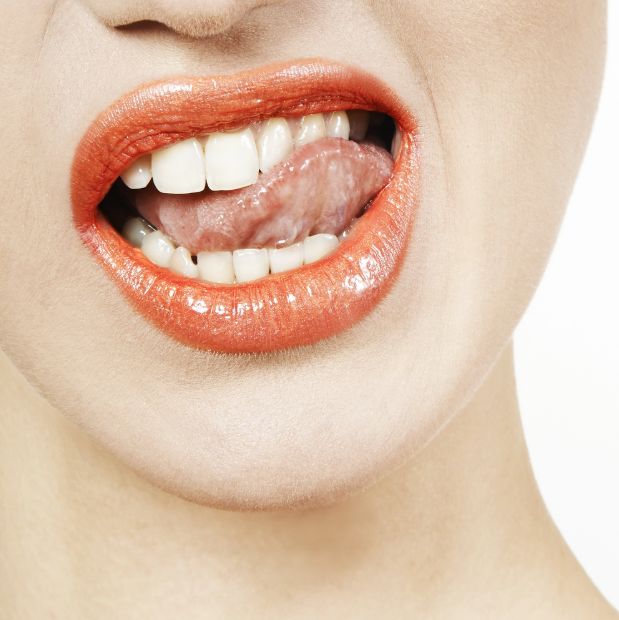 may26b Close-up of lips with red lipstick, teeth showing while tongue touches the lips in a playful pose.